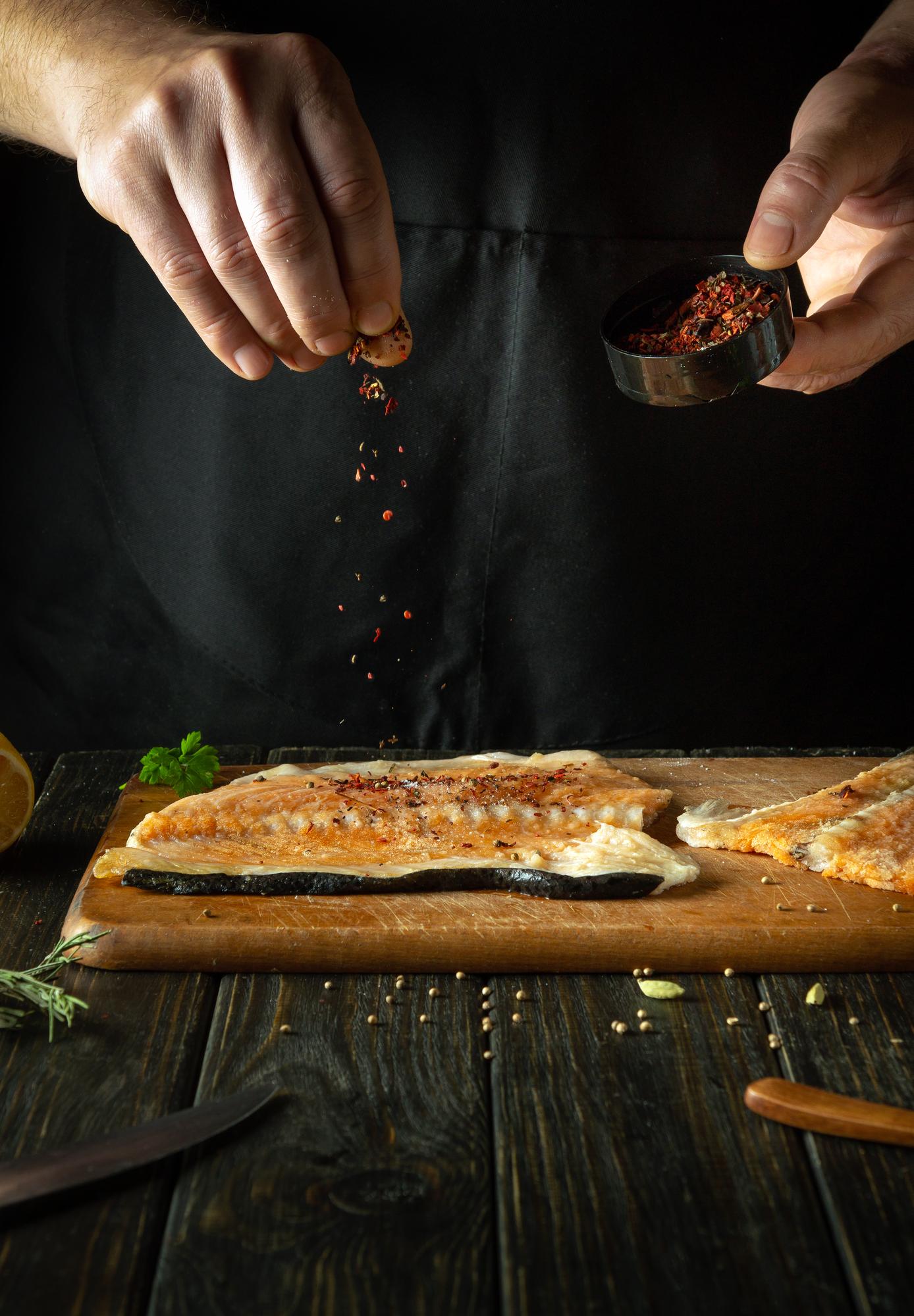 Hands seasoning a pan-seared fish